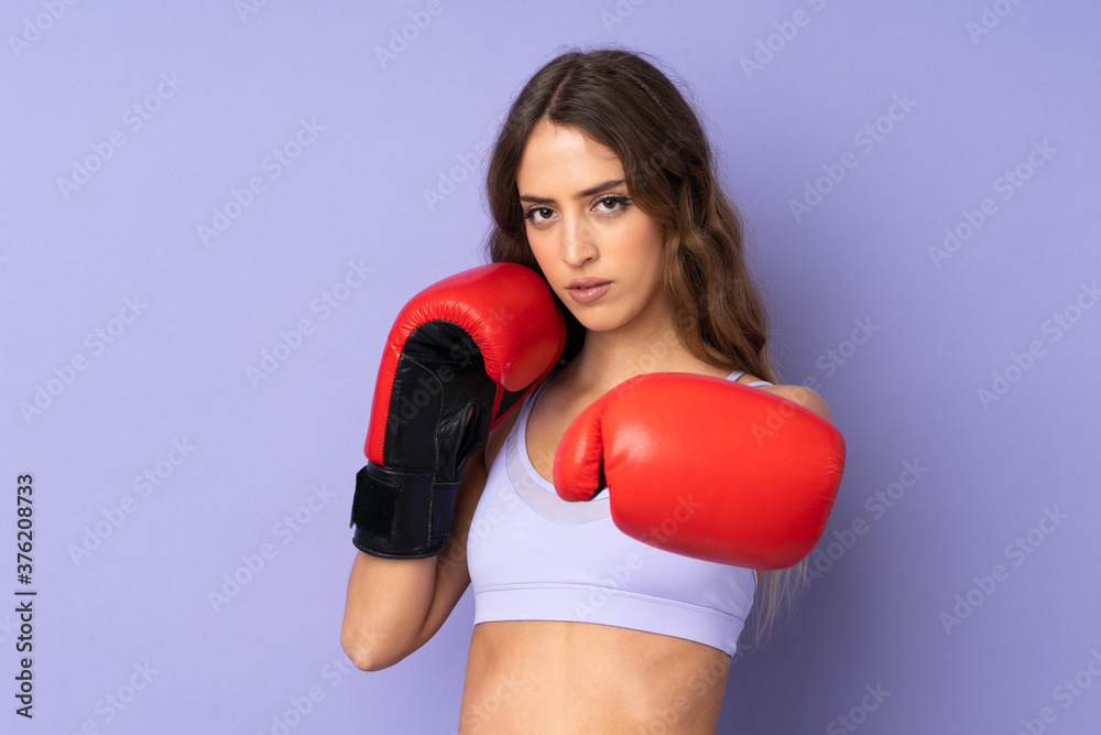 Young sport woman over isolated purple background with boxing gloves