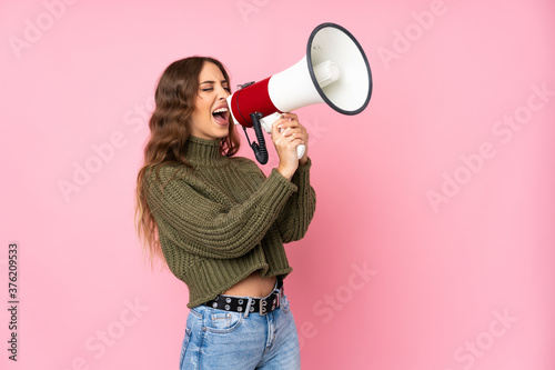 Young woman over isolated pink background shouting through a megaphone