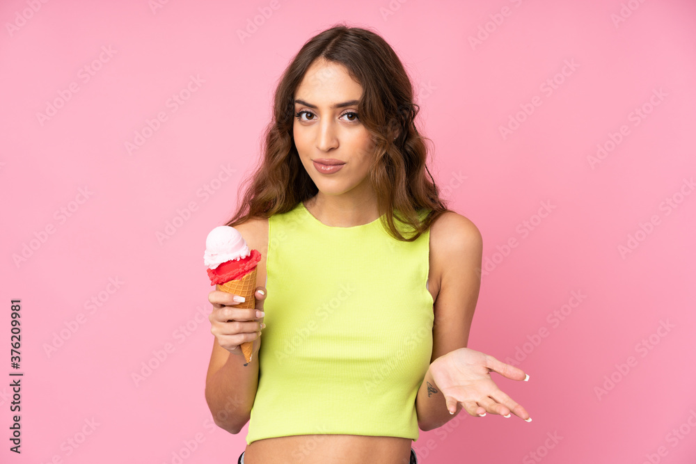 Young woman holding a cornet ice cream over isolated on a pink background making doubts gesture while lifting the shoulders