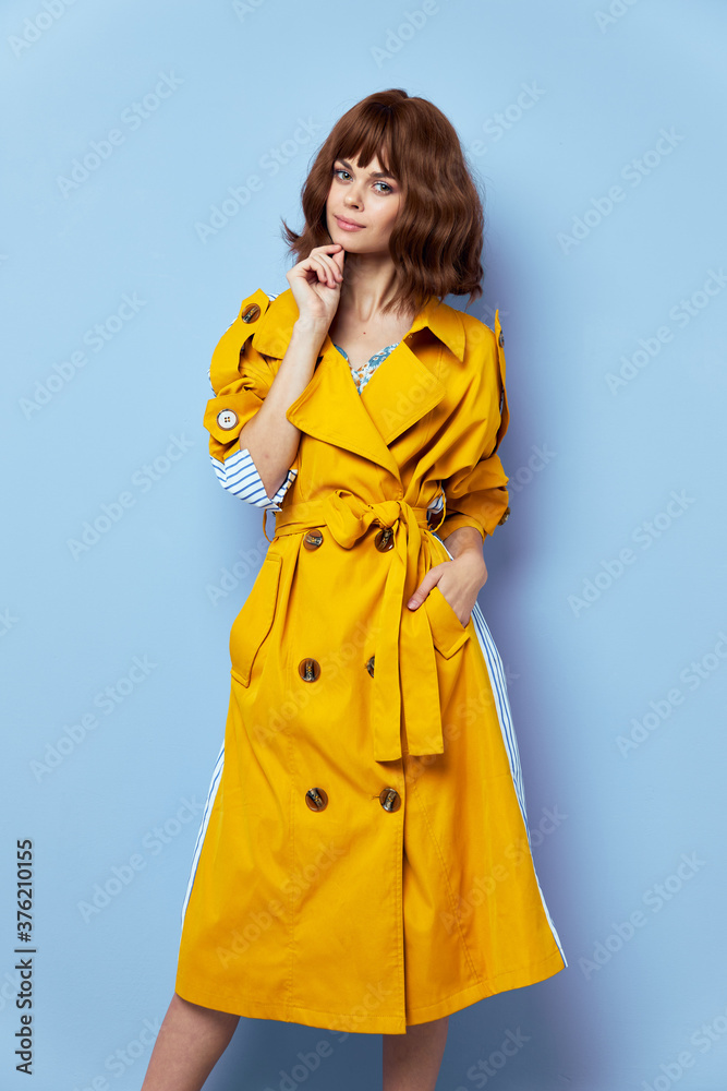 Lady in a fashionable coat on a blue background full growth touches her face Lady in a fashionable coat on a blue background full growth touches her face