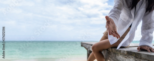 Asian woman sitting on wooden terrace at a tropical beach and stretch her hand to invite tourists to travel the sea.
