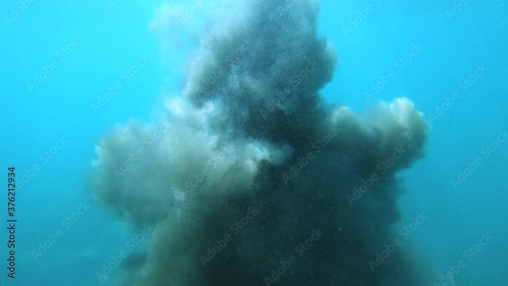 Cloud of dust erupt under the water. Fine sand floating underwater. Sunbeams shining on seabed floor. Diving in shallow ocean water. Wide angle, slow motion