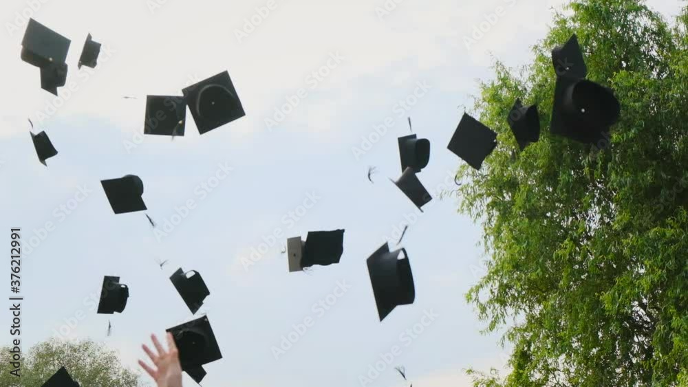 High school students graduate throwing graduation square academic cap bonnet into the sky in slow motion, education college ceremony in front of threes. Hands catching hats after finishing university