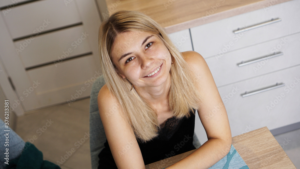 Cheerful young female sitting at table in cozy styled room while smiling and looking at camera Cheerful young female sitting at table in cozy styled room while smiling and looking at camera