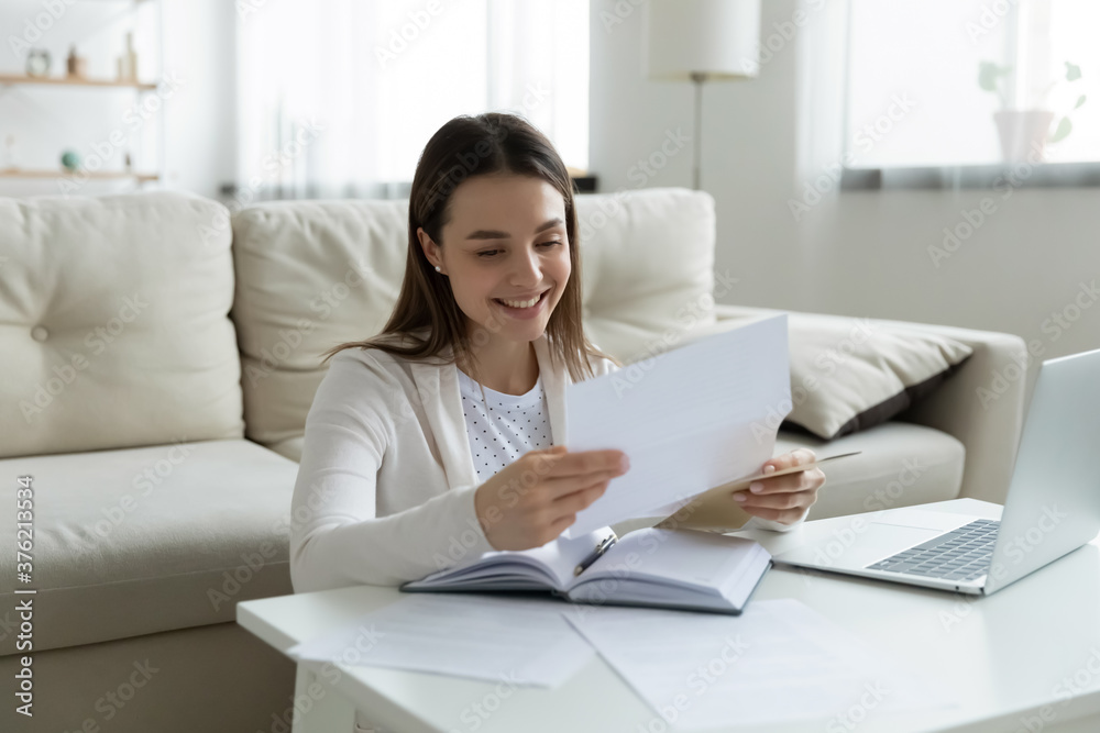 Smiling young woman reading unwrapped from paper envelope letter, excited by good news. Happy millennial girl checking post mail, received bank tax refund notification or loan approval at home. Smiling young woman reading unwrapped from paper envelope letter, excited by good news. Happy millennial girl checking post mail, received bank tax refund notification or loan approval at home.