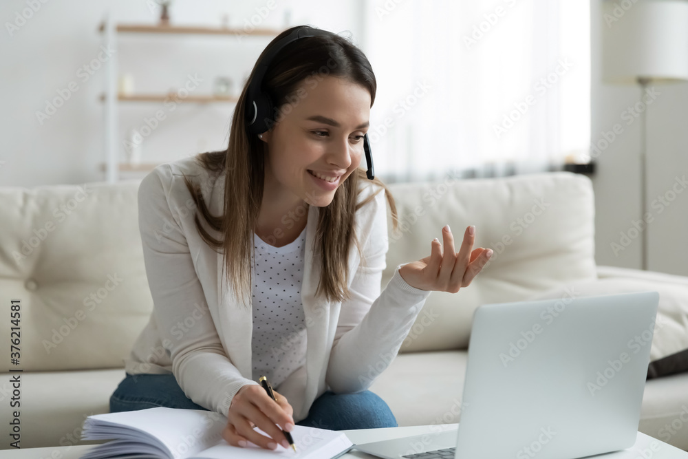 Happy young beautiful female student in wireless headphones with microphone enjoying studying remotely. Cheerful millennial woman looking at computer screen, giving educational class to client online. - obrazy, fototapety, plakaty 