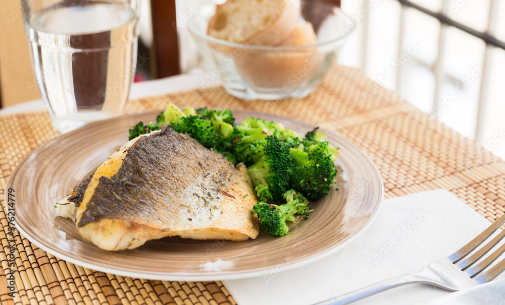 fried fillet of sea bass with garnish of broccoli on black warm stone plate fried fillet of sea bass with garnish of broccoli on black warm stone plate
