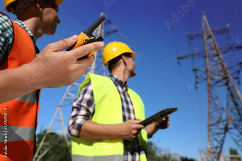 Professional electricians near high voltage towers, focus on hand with portable radio station © New Africa