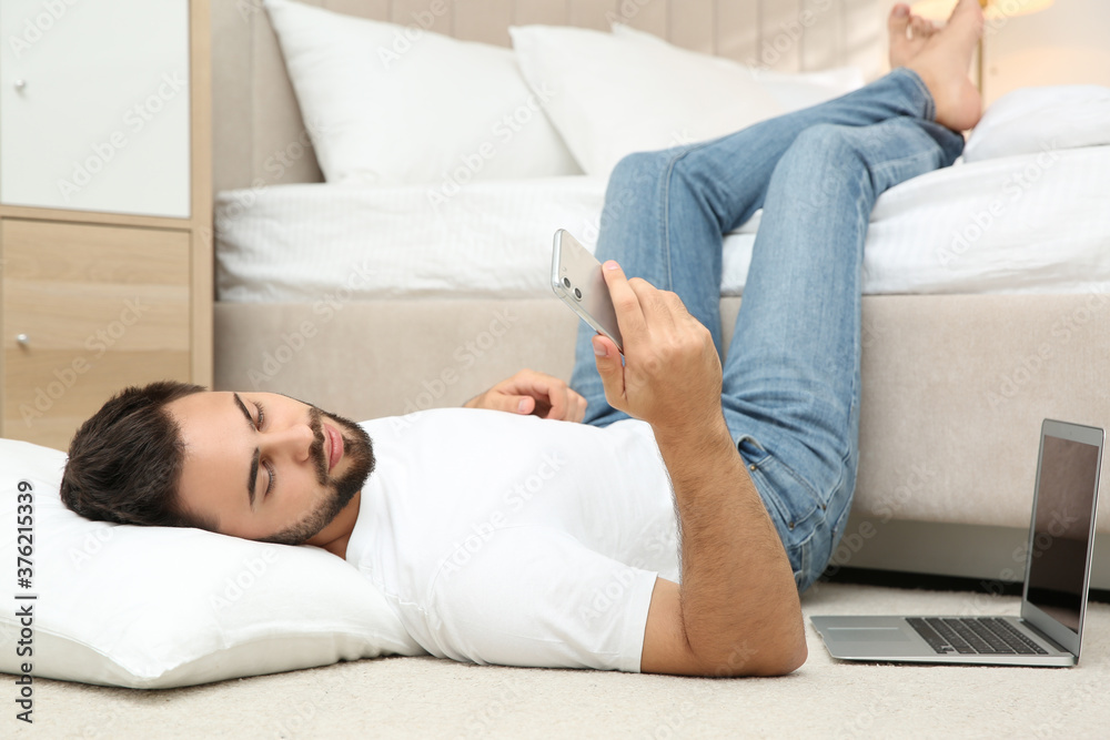 Lazy young man with laptop and smartphone lying on floor at home Lazy young man with laptop and smartphone lying on floor at home