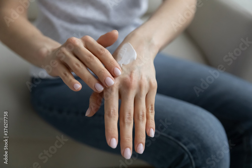 Close up young woman applying moisturizing balm on hands, taking care of dry skin, making it healthy and soft. Lady enjoying daily skincare spa procedures, moisturizing body parts with organic cream.