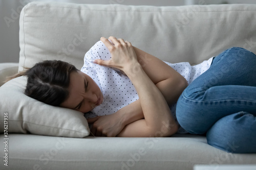 Quadro em tela Stressed young woman lying on sofa, embracing shoulders with arms, suffering from depression alone at home or caught cold and shivering