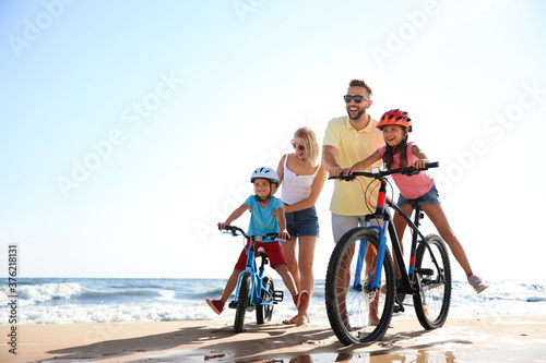 Fototapeta Naklejka Na Ścianę i Meble -  Happy parents teaching children to ride bicycles on sandy beach near sea