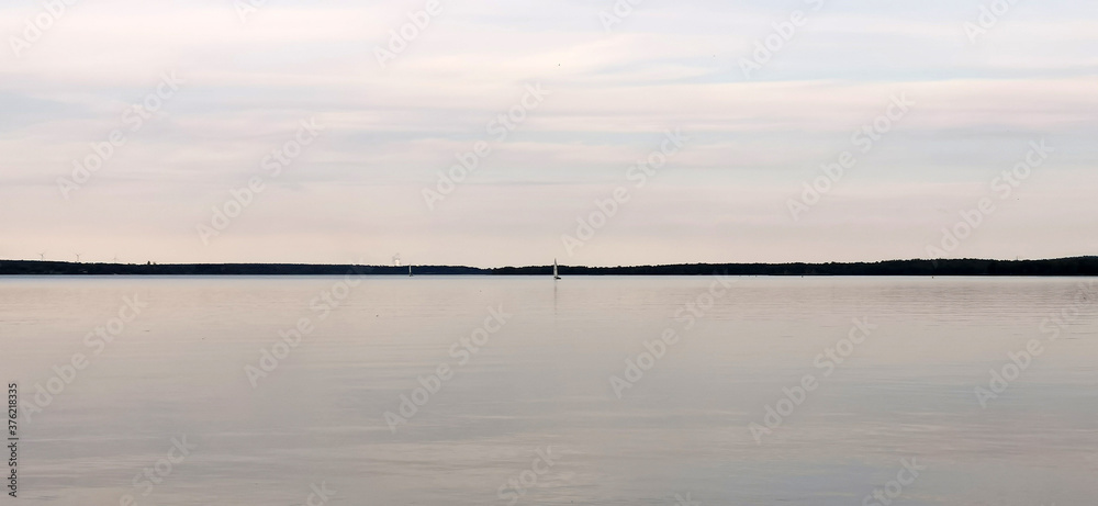 Ruhiger See mit einem Segelboot in der Ferne am weiten Horizont