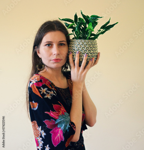 Beautiful young woman in a boho dress with kimono sleeves in a colorful floral pattern with a climbing plant with twisted leaves - Epipremnum, in a designer pot photo