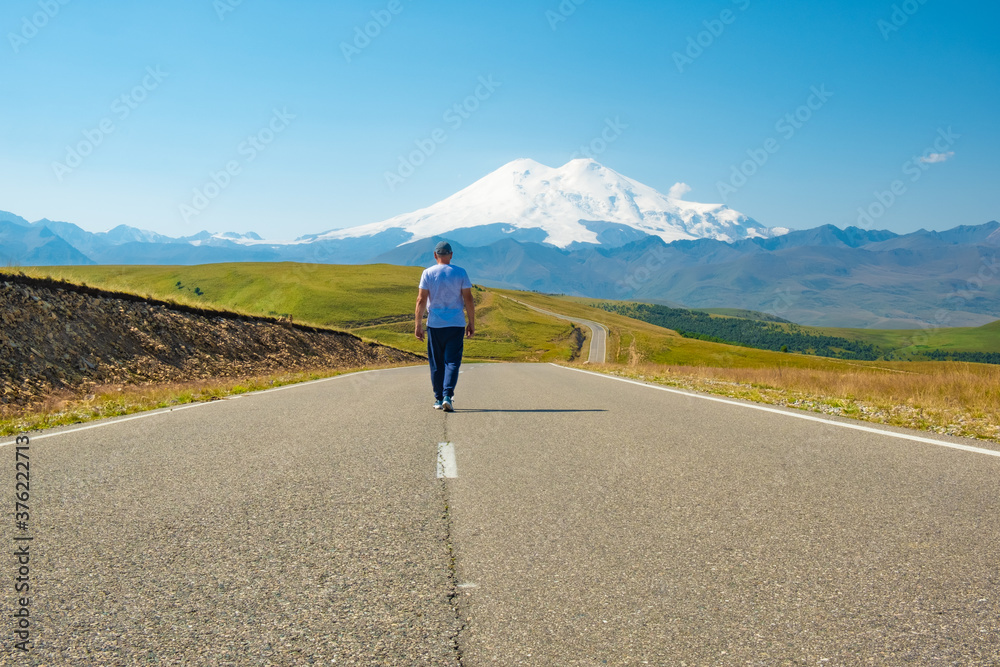 A man walks along the highway against the background of Mount Elbrus, Caucasus Russia. The concept of travel and freedom