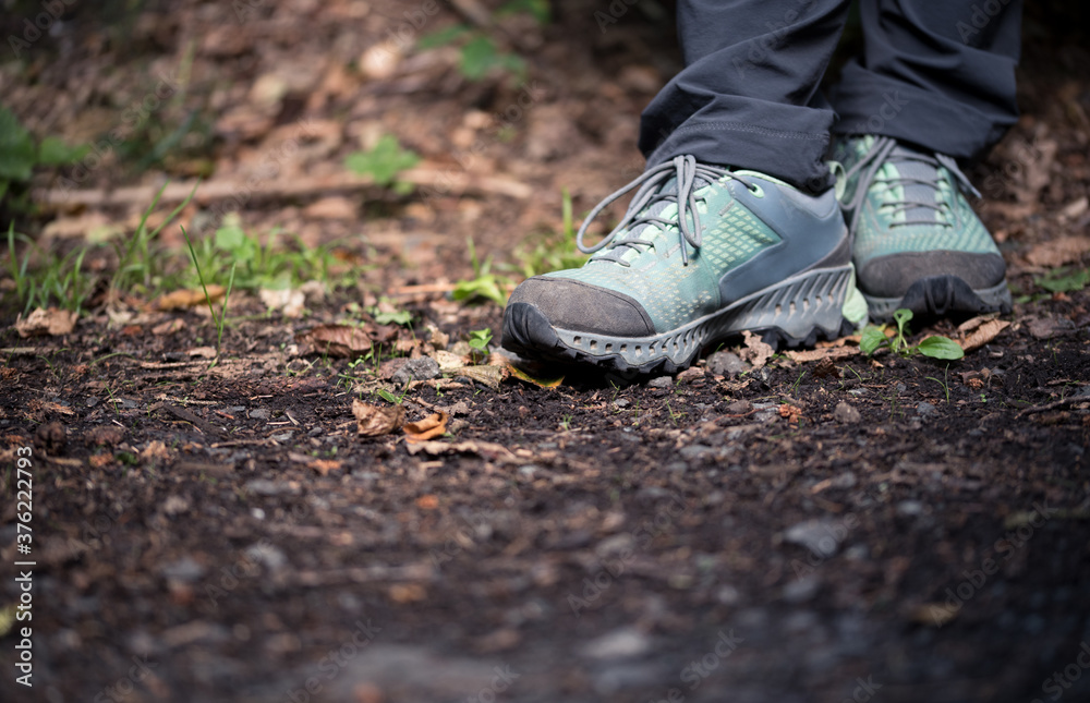 Close-up of legs and turquoise trekking shoes standing on a forest soil with space for text in the front