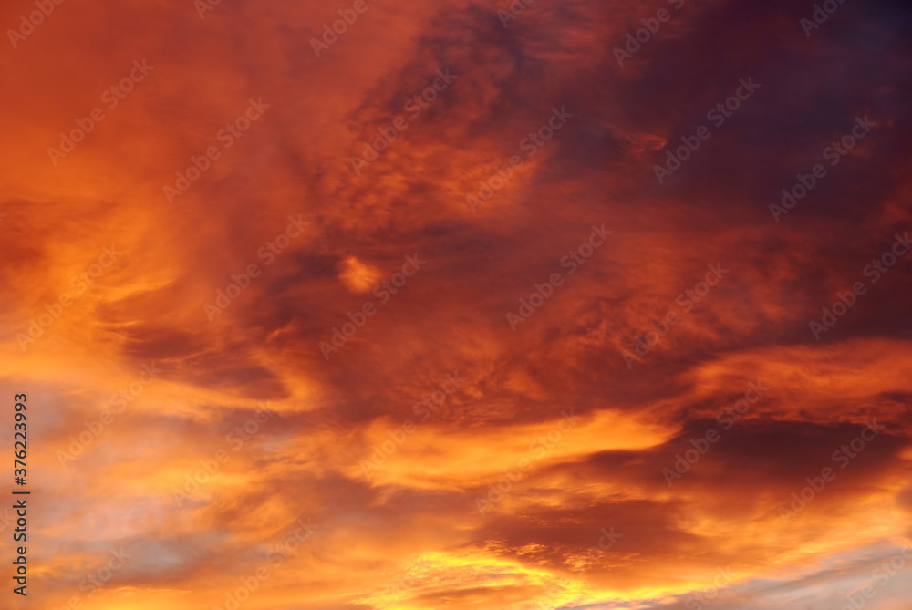 Dark blood red sky background. Dramatic heavy clouds with the hint of the sun at sunset. Many orange tones and patterns of clouds.