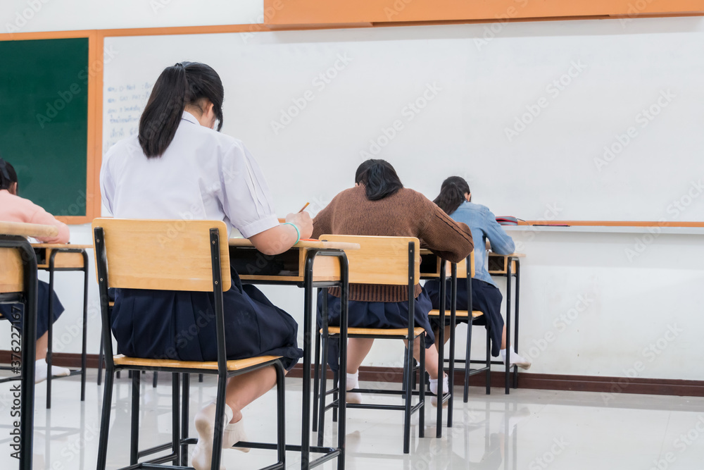 Writing test in exam with behind girl Asian students group concentrate in high school, serious taking final examination desk at classroom with Thai student uniform. Education evaluation concept Writing test in exam with behind girl Asian students group concentrate in high school, serious taking final examination desk at classroom with Thai student uniform. Education evaluation concept