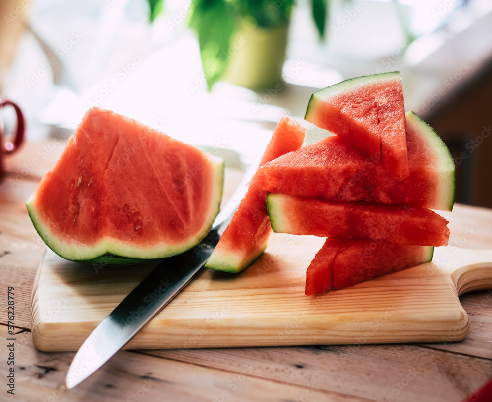 Closeup view of ripe fresh watermelon slices on a cutting board on wooden table, steel knife Closeup view of ripe fresh watermelon slices on a cutting board on wooden table, steel knife