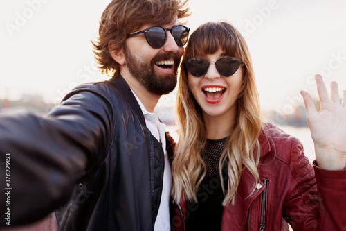 Attractive stylish couple in love posing outdoor, hugging and walking on quay. Soft evening colors. Fashionable look. Trendy sunglasses. Man and woman embarrassing.