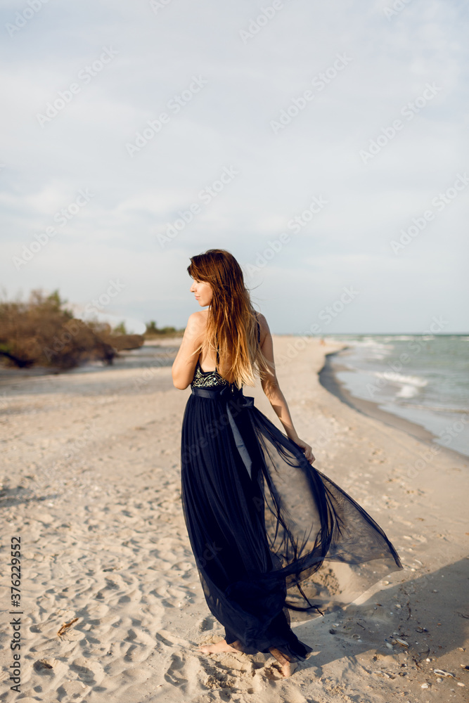 Full height image of Fashionable woman in elegant luxury dress posing on  the beach. View from back. Long hairs. Stock-Foto | Adobe Stock