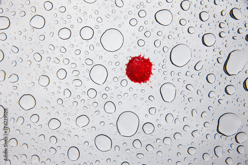 Wassertropfen und Roter Tropfen auf einer Glasscheibe