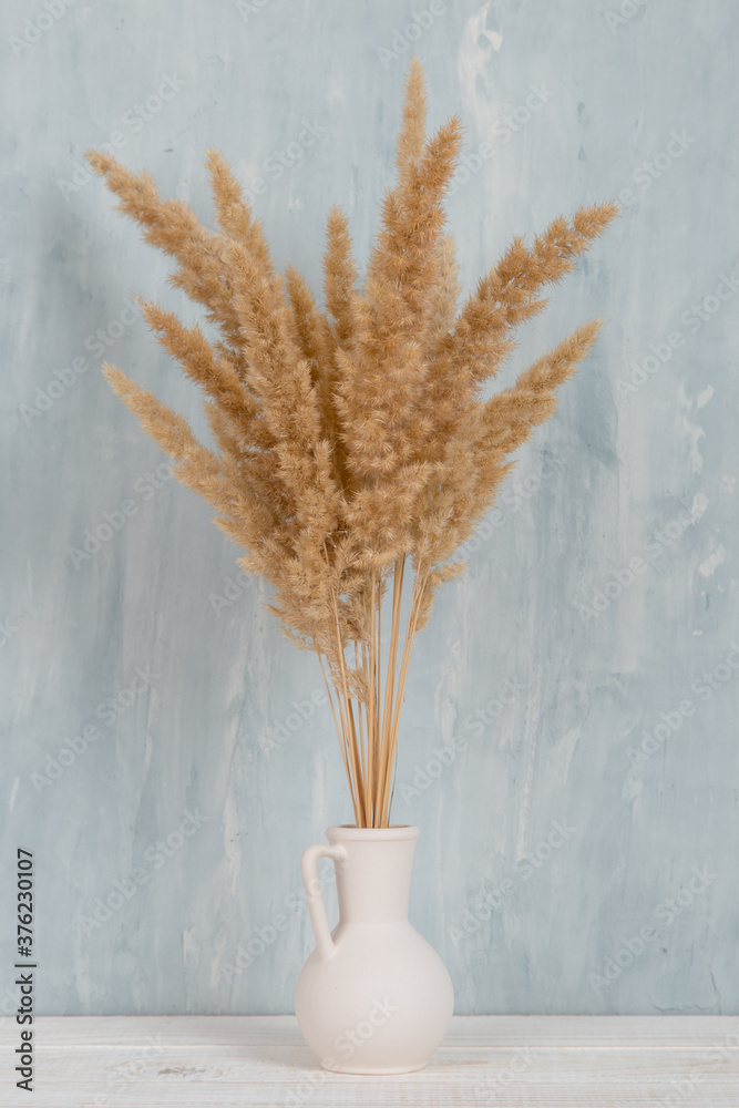 Plakat A vase with yellow spikelets on the table, on a blue background. Light stylish design.