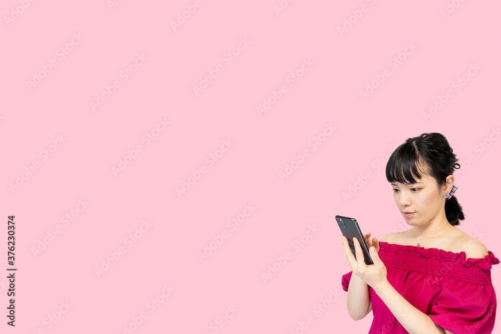 スマホを操作する女性(ピンク背景) スマホを操作する女性(ピンク背景)
