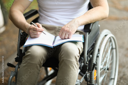 Man in wheelchair sits and holds notebook and pen. Learning professions of people with disabilities concept