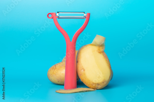Red vegetable peeler and potatoes on a blue background photo
