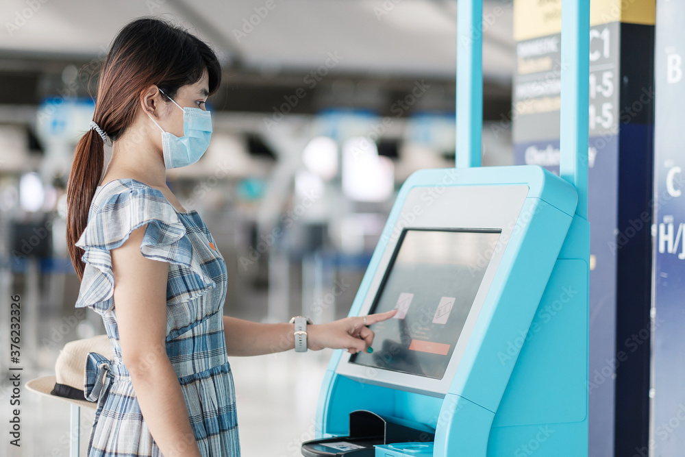 Φωτογραφία woman wearing medical face mask and using the self check-in machine at the airport terminal getting the boarding pass, Asian woman traveler ready to travel