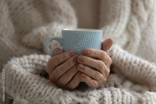Close up mature woman wrapped warm blanket holding mug of coffee or tea, middle aged female enjoying free time, weekend at home, relaxing, drinking hot beverage in morning, starting new day