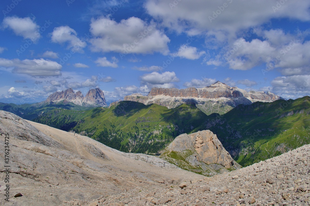 Beautiful landscape of Dolomites mountains, Langkofel, Sella group. Sunny day, blue sky, white clouds, rocky road in foreground. 