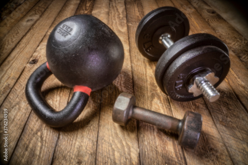 heavy iron kettlebell and dumbbells on a rustic wood background - fitness concept, soft focus image shot with lensless pinhole camera
