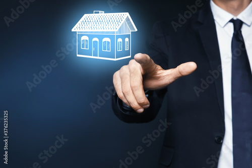 Real estate agent touching house illustration on virtual screen against dark background  closeup