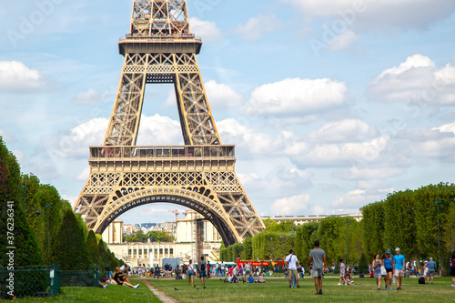 Paris, France. 2019, August. The Eiffel tower on Champ de Mars with tourists around the park un a cloudy summer day.