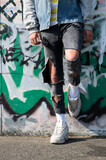 One teenager with ripped black jeans and white sneakers leaning against a graffiti wall. Urban street wear. Skate track youth hangout. Modern city fashion of the netherlands. 