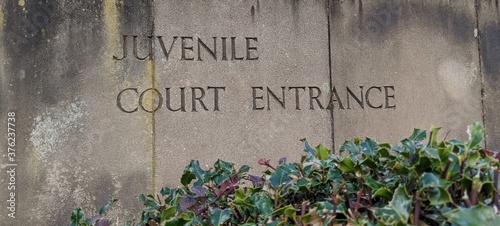 Weathered stone slab sign with the words juvenile Court Entrance engraved into it with foliage at the bottom Outside the Department Of Justice courthouse where juveniles are tried.  photo