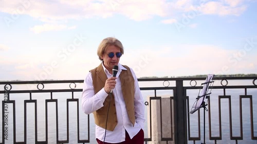 portrait of a young man who sings a song from the outside, a professional singer opens his mouth to music in the daytime on the street, hand of person holding a microphone