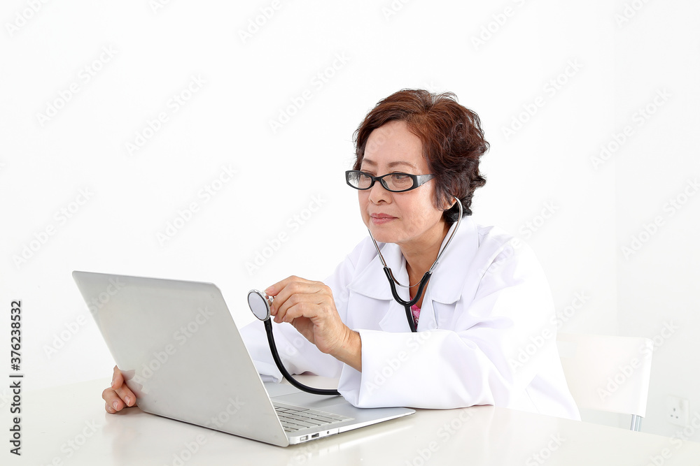 Elderly asian Chinese female doctor on white background wearing white apron checking diagnostics on notebook laptop pc with stethoscope Elderly asian Chinese female doctor on white background wearing white apron checking diagnostics on notebook laptop pc with stethoscope