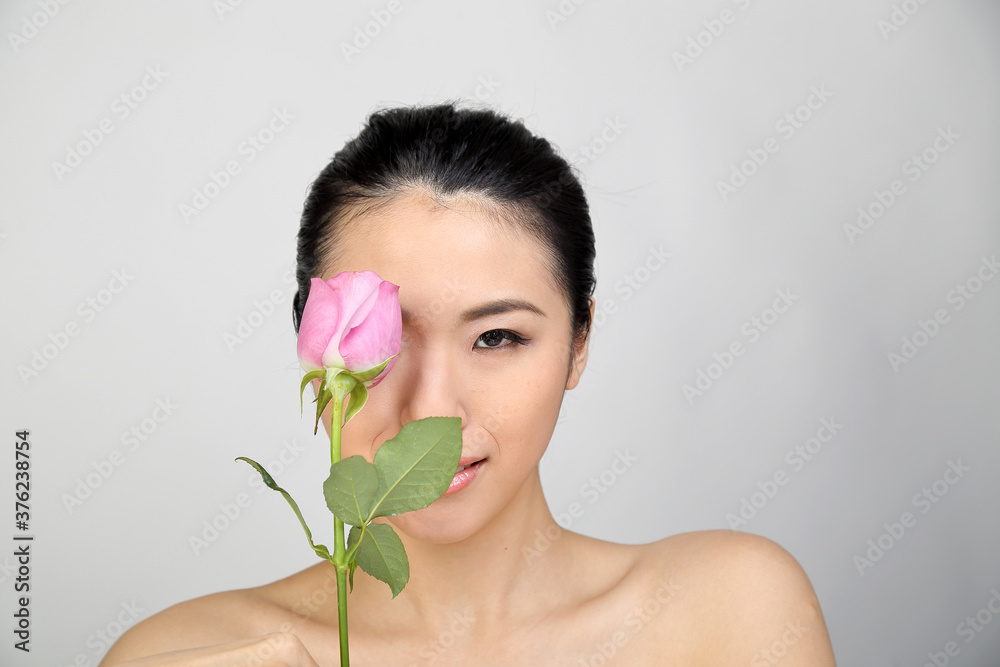 Young beautiful Southeast Asian woman beauty fashion makeup light grey white background holding pink rose over eye face