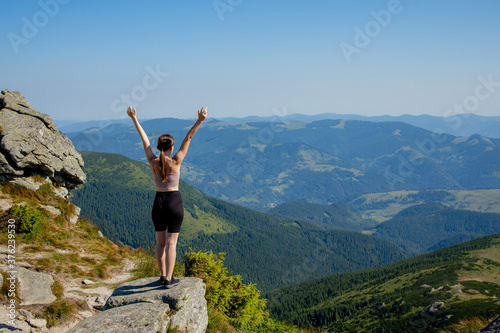 The young girl at the top of the mountain raised her hands up on blue sky background. The woman climbed to the top and enjoyed her success. Back view © volody10