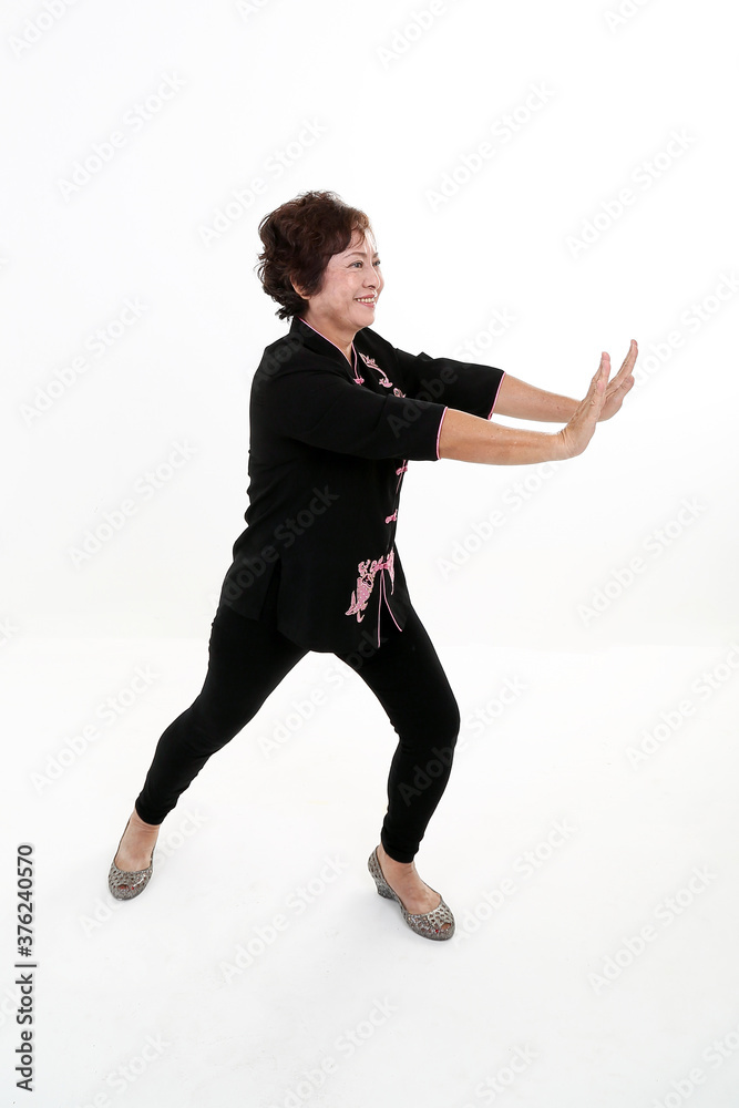 Elderly asian Chinese female wearing black tang samfu on white background exercise tai chi