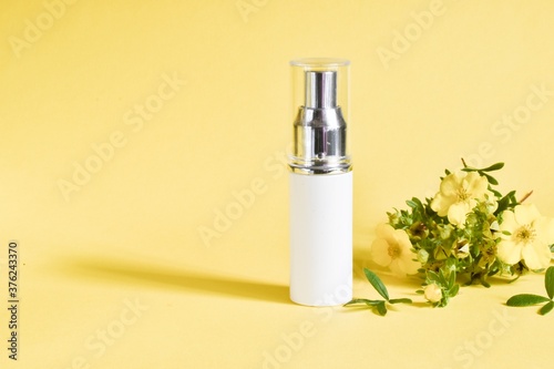 White tube for cosmetic products. Blank plastic container for cream, lotion, toothpaste, nourishing or moisturizing mask with yellow flowers on a yellow background.Copy space