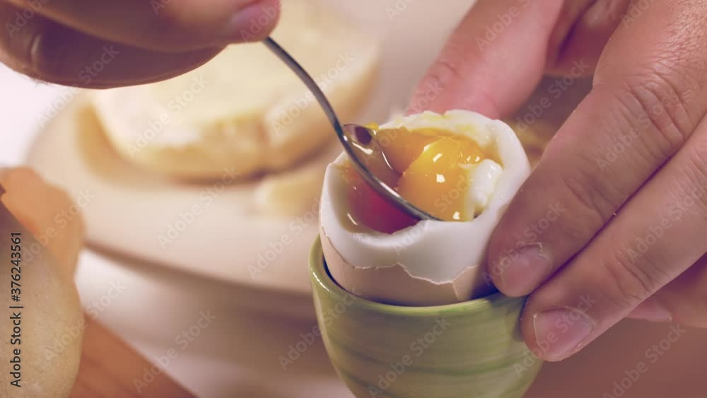 Person eating soft boiled egg for breakfast.