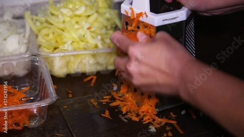 Human hands grate raw carrot on a metal grater for making soup or salad. Rubbing carrot. Cooking vegetarian healthy food. Close-up
