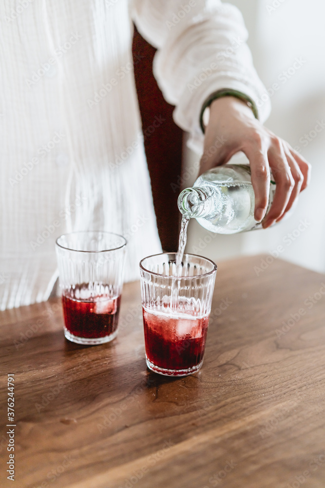 a hand is pouring soda into two glasses of iced drinks a hand is pouring soda into two glasses of iced drinks