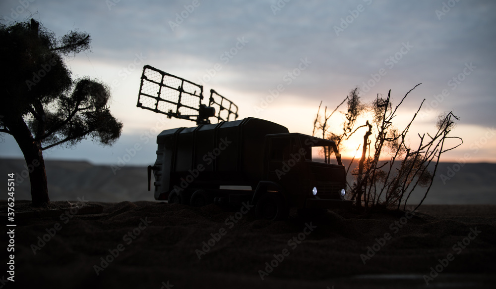 Fototapeta premium Silhouette of mobile air defence truck with radar antenna during sunset. Satellite dishes or radio antennas against evening sky.