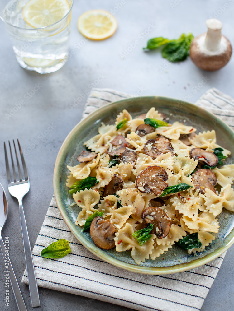 farfalle with mushrooms and spinach on a gray concrete background. vertical image