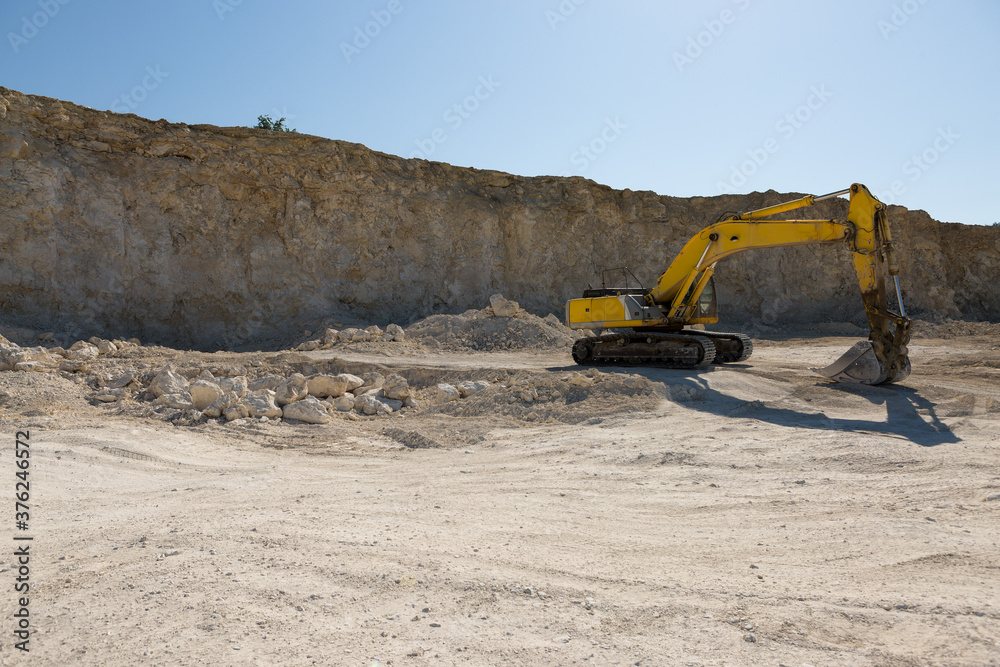 A large yellow tracked excavator is mining rock in a quarry. A large yellow tracked excavator is mining rock in a quarry.